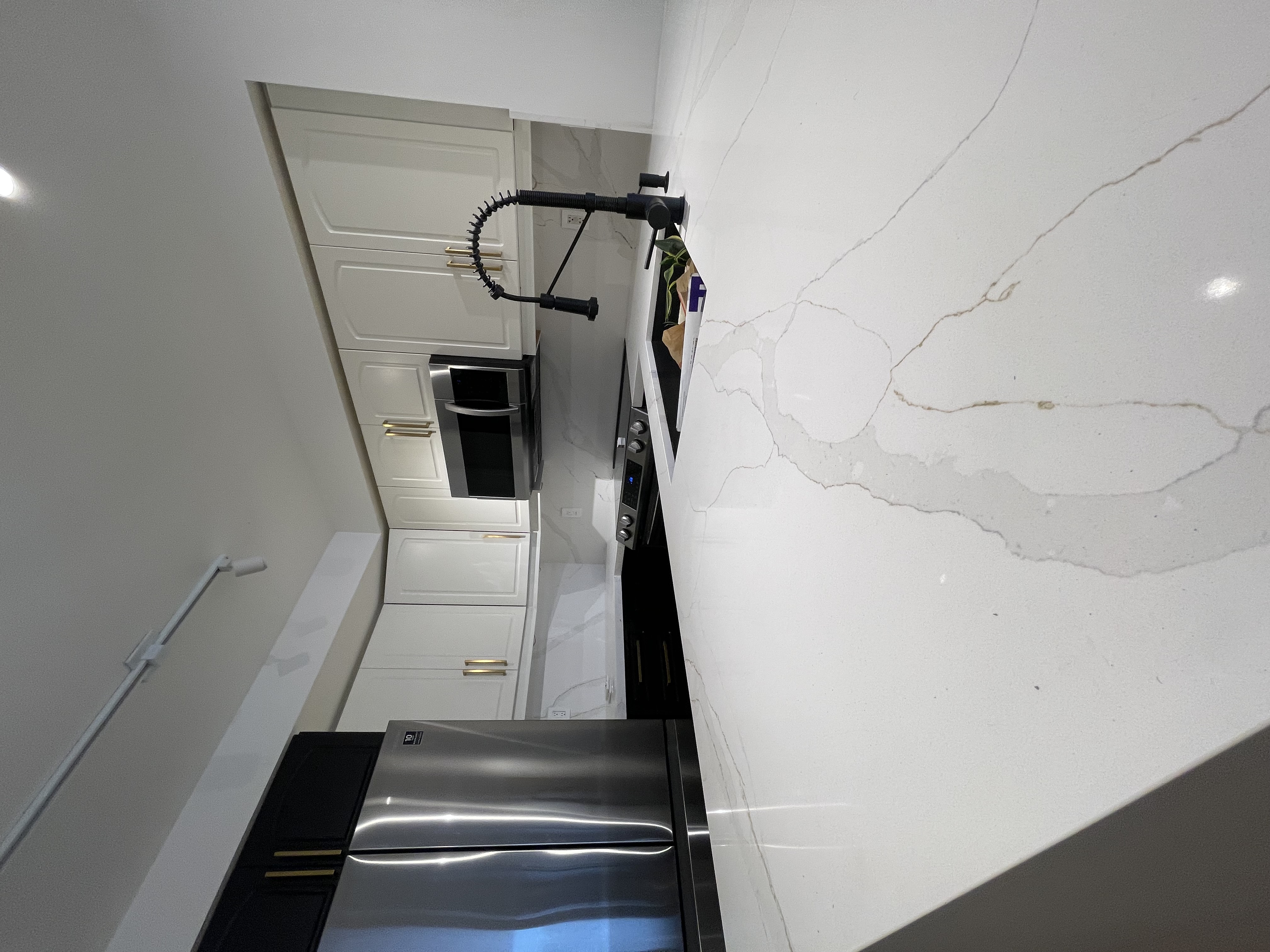 Clean finished kitchen with dramatic quartz veining and good material contrast — strong portfolio shot despite artificial lighting — Queensway, Hamilton | MTC Renovations
